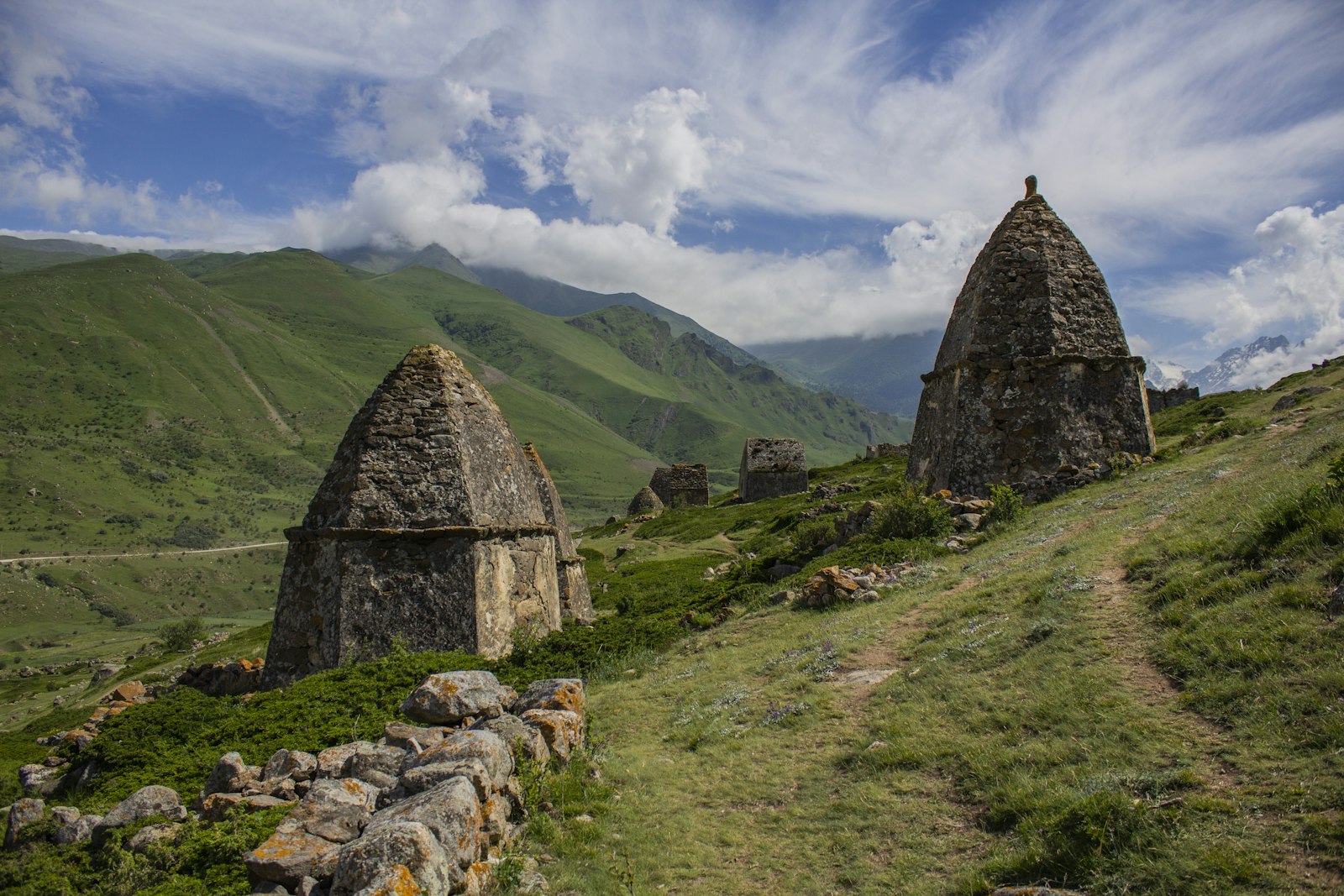 gray concrete house on green grass field near mountain under white clouds and blue sky during