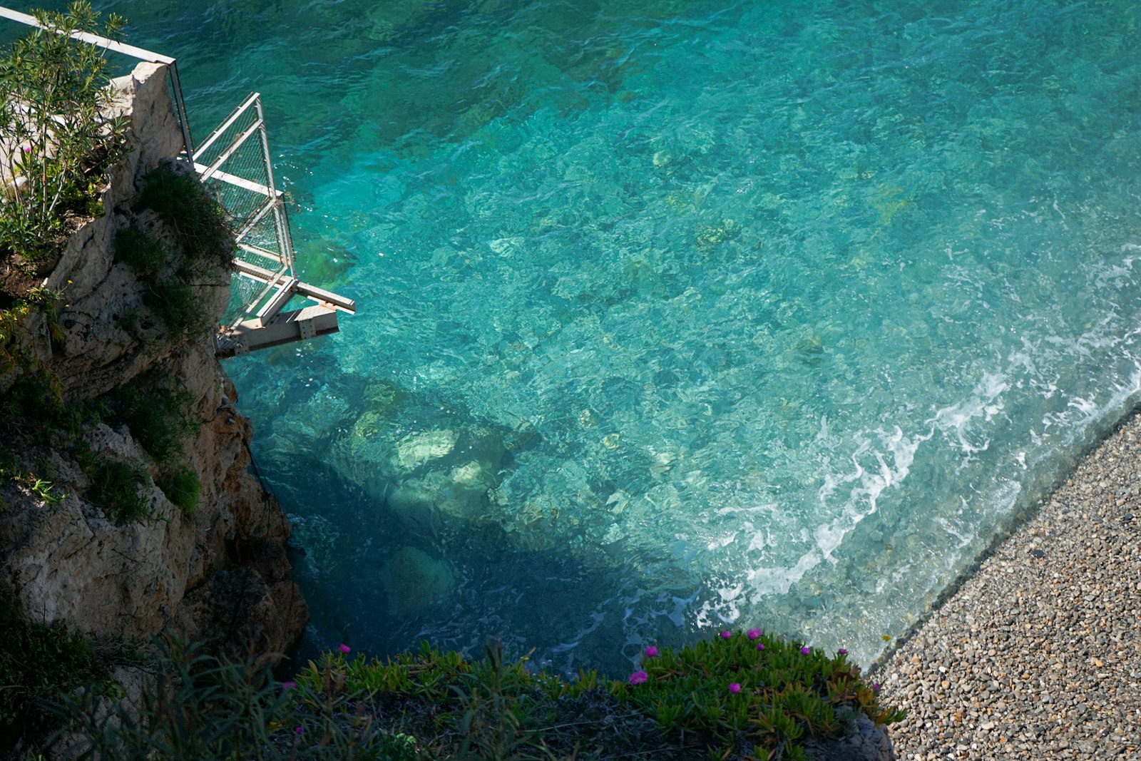 Clear turquoise sea by a rocky cliff and pebble beach.